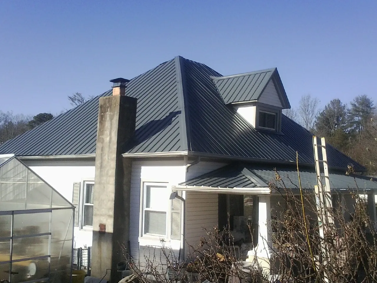 Dark blue standing seam metal roof on a white farmhouse with dormer — Slate & Tile Roof Repair by Roofing Brothers in Sharps Chapel