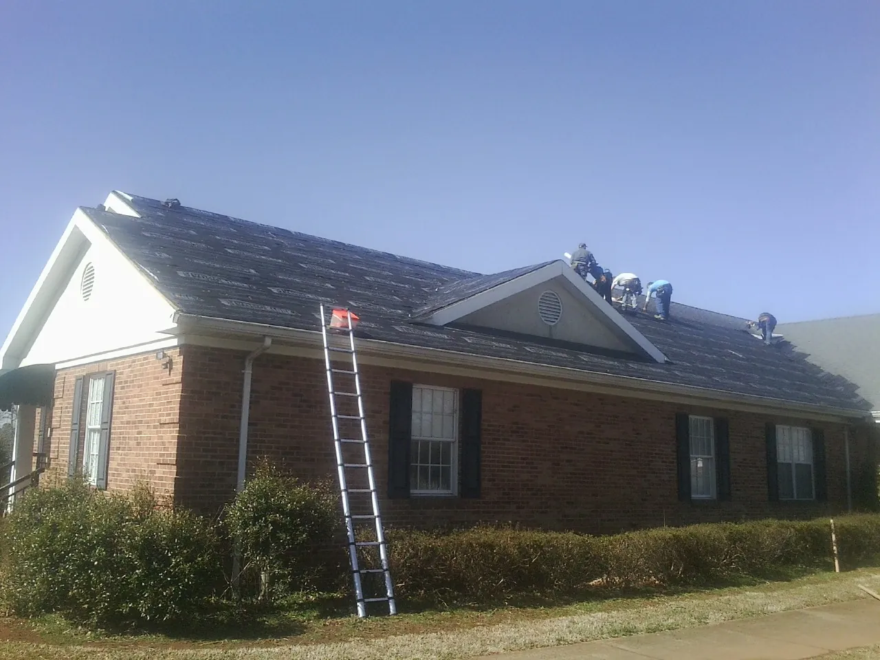 Crew tearing shingles off a brick ranch roof with a ladder set — Emergency Roof Repair work by our crew in Sharps Chapel