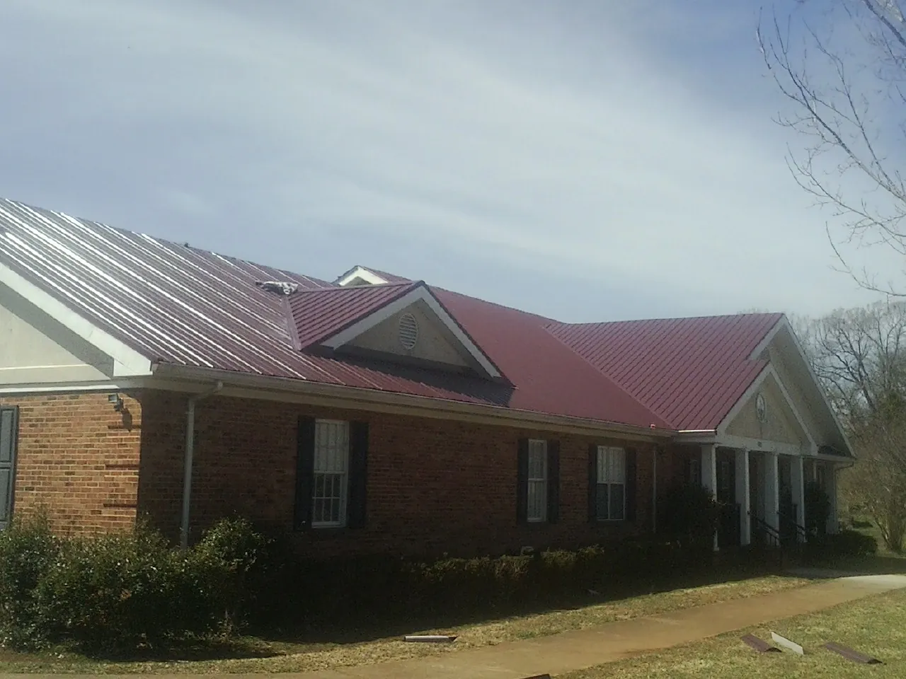 Red metal roof with gabled entries on a long brick building, from a Hail Damage Roof Repair job in Sharps Chapel