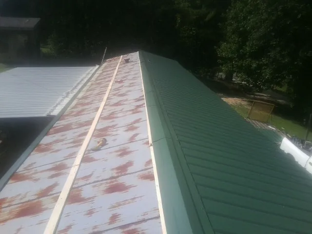 Old rusted panels beside newly installed green metal roofing — Wind Damage Roof Repair by Roofing Brothers in Sharps Chapel