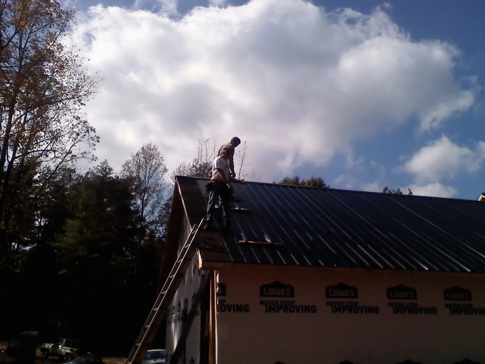 Roofer fastening dark metal panels high against a cloudy sky, from a Roof Inspection job in Sharps Chapel