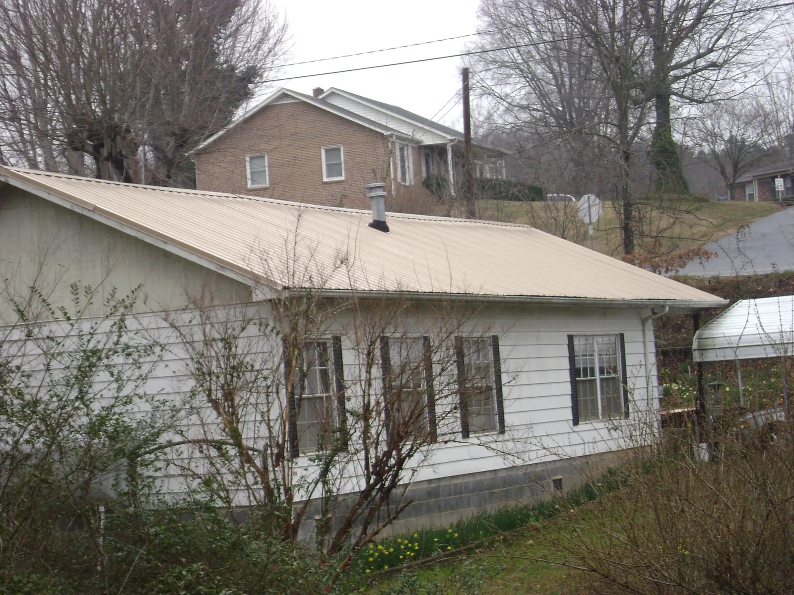 Tan metal roof on a white sided house set into a hillside — Commercial Roofing by Roofing Brothers in Sharps Chapel