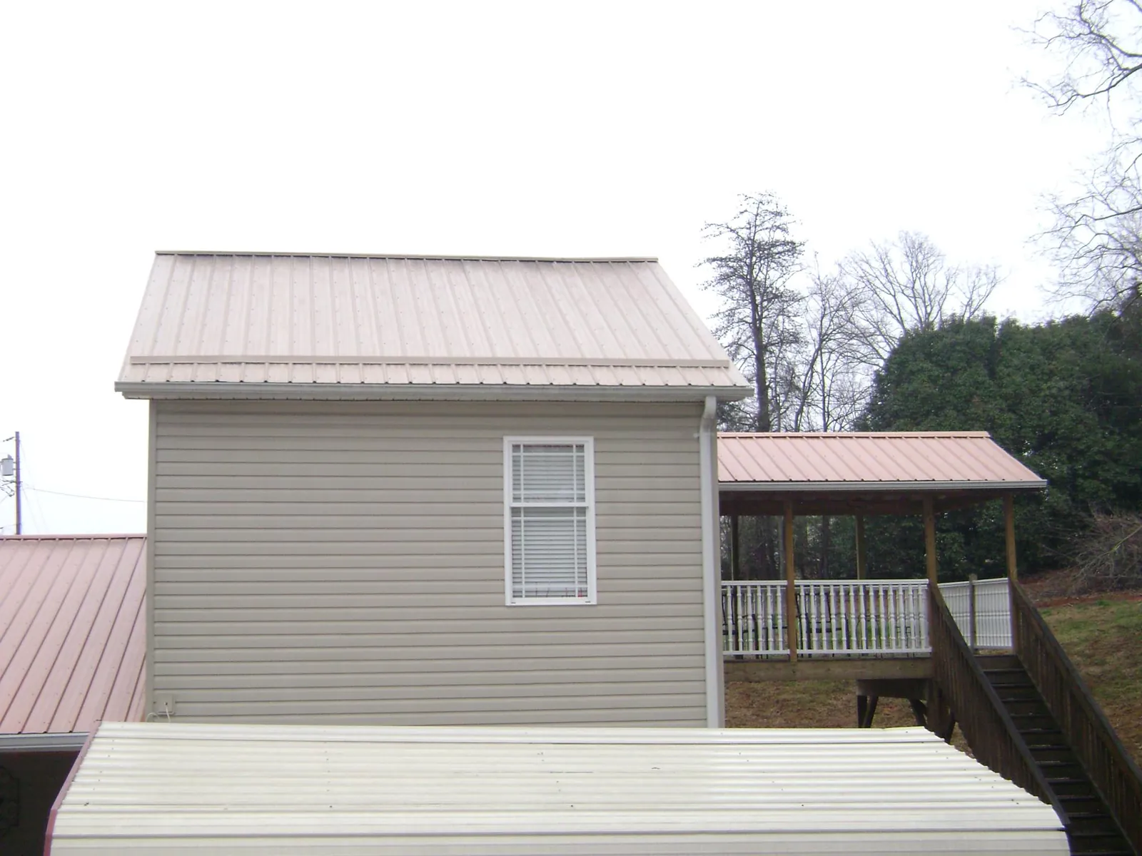 Tan metal roofs on a two story addition and attached porch, from a Roof Replacement job in Sharps Chapel