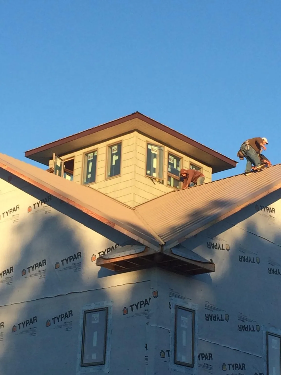 Roofers working around a rooftop cupola on a new metal roof at sunset — Roof Waterproofing in Sharps Chapel by Roofing Brothers